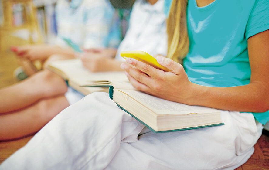 Childrens hand holding smartphone over open book Jóvenes de la generación punto X a la generación Alpha
